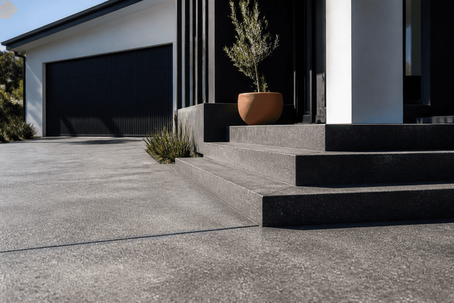 Charcoal concrete driveway meeting entry steps and planted garden beds